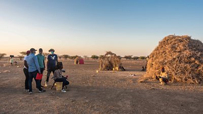 A BBC Media Action crew films a man sitting in front of his thatched house in an arid landscape in northern Kenya
