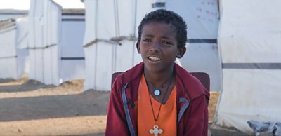 A young boy in a red sweater and orange T shirt faces the camera