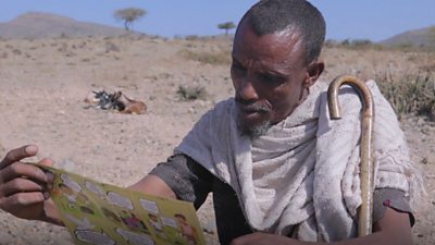 Mohamed a shepherd looks at a pamplet explaining the dangers of explosive ordnance