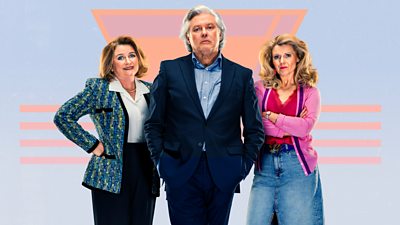 A man stands with two women by his side. They are all wearing slightly nineties style clothing. He wears a suit, the woman on his left wears a blazer over a blouse while the woman on his right wears a cardigan over a red top and denim skirt.